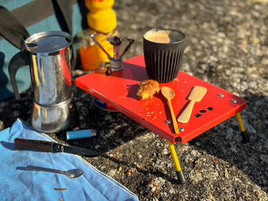 Camp Stove Table in Traffic Red on a rock with a coffee cup and a Bialetti coffeepot